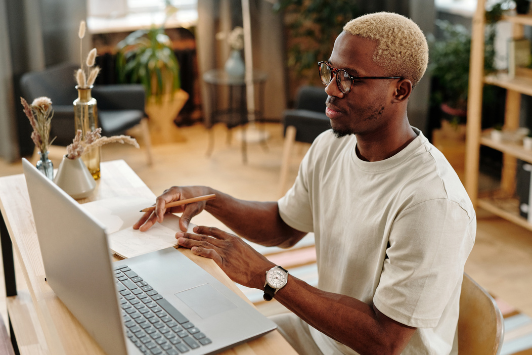 Man in White Shirt Holding Brown Pencil while using Laptop